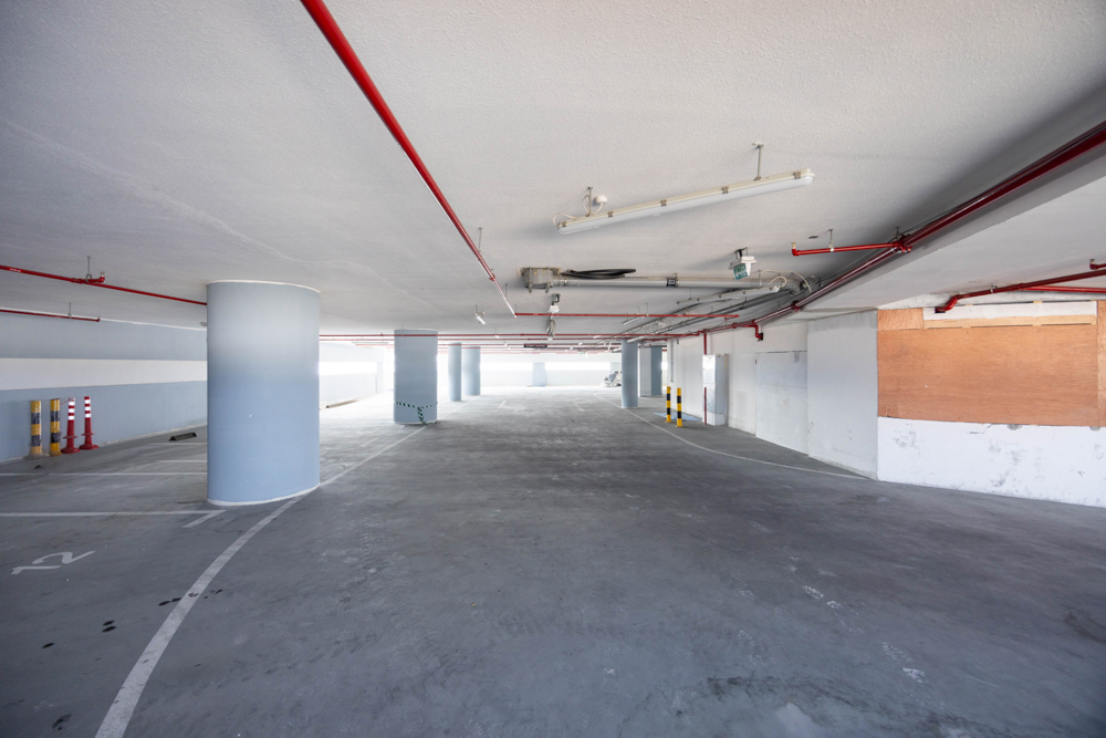 Beach Walk Residence A spacious underground parking area with concrete flooring, pillars, and visible red piping along the ceiling.